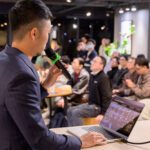 梁文宣手持麥克風面向觀眾分享全端寫作系統，觀眾專注聆聽