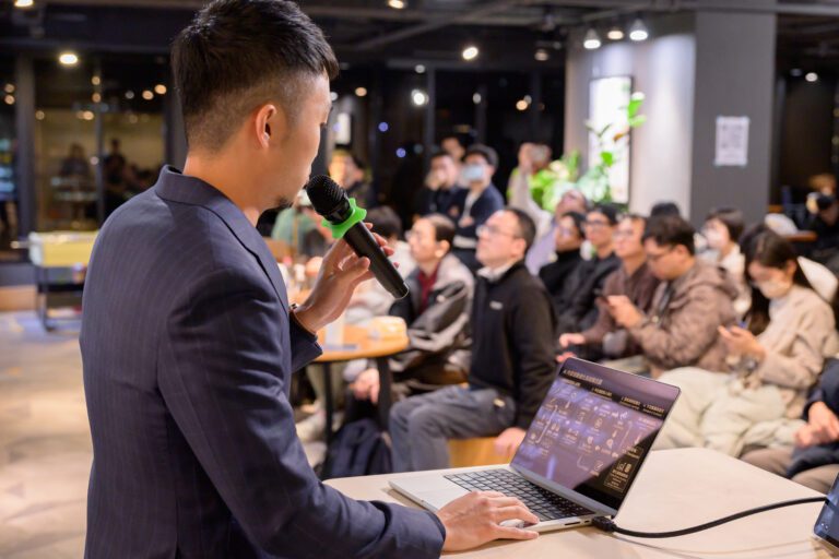 梁文宣手持麥克風面向觀眾分享全端寫作系統，觀眾專注聆聽